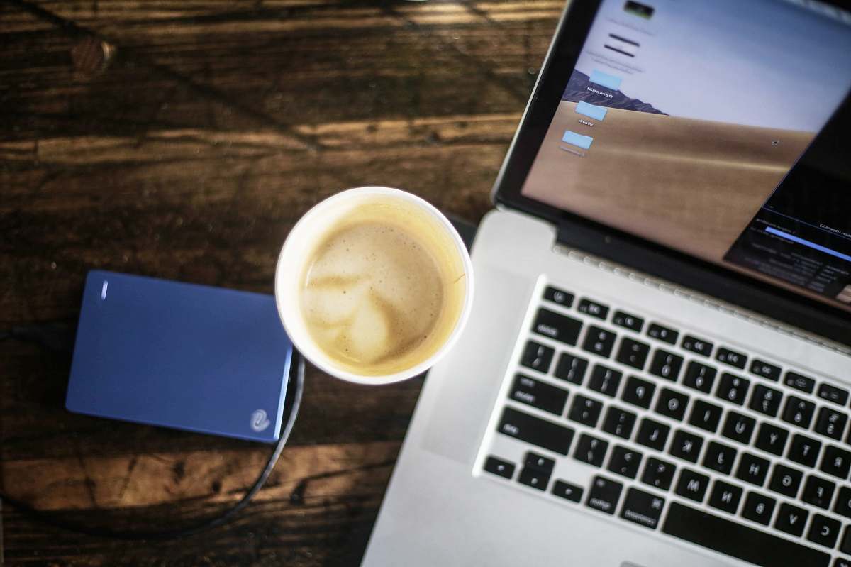 computer hardware cup of coffee latte between turned-on laptop and Seagate portable drive computer keyboard
